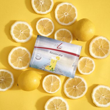 Restorate Eine Packung mit Limondrinkmix umgeben von frischen Zitronenscheiben auf gelbem Hintergrund.